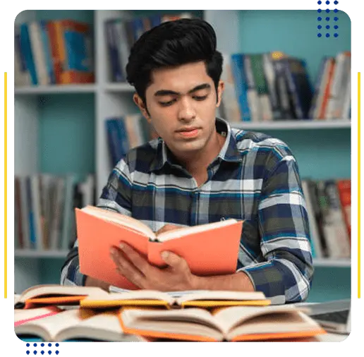 A male student studying in a library with books, representing popular courses in the UK for international students