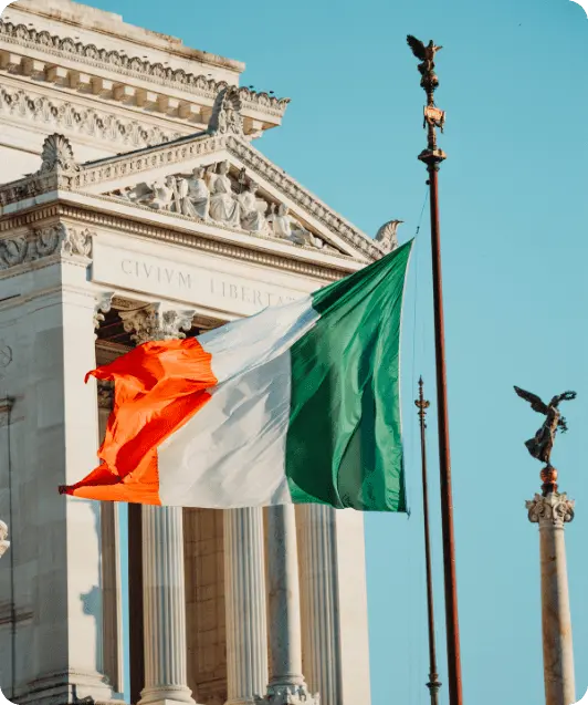 The front of a large historical stone building, likely Trinity College Dublin, under a partly cloudy sky